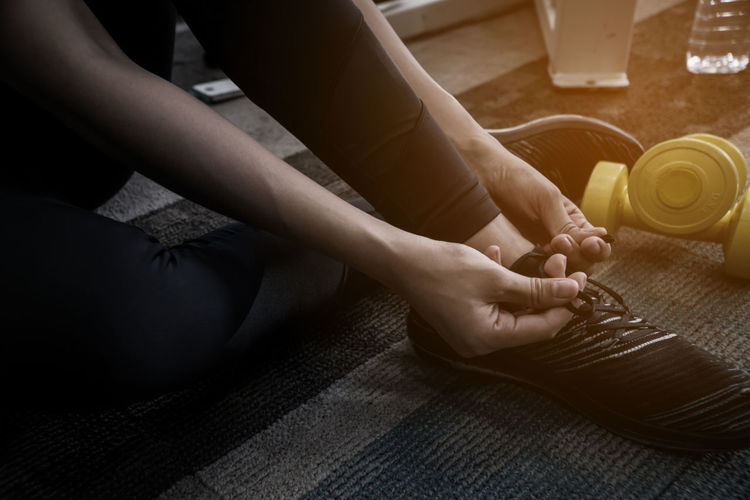 Low section of woman tying shoelace while sitting on carpet in gym