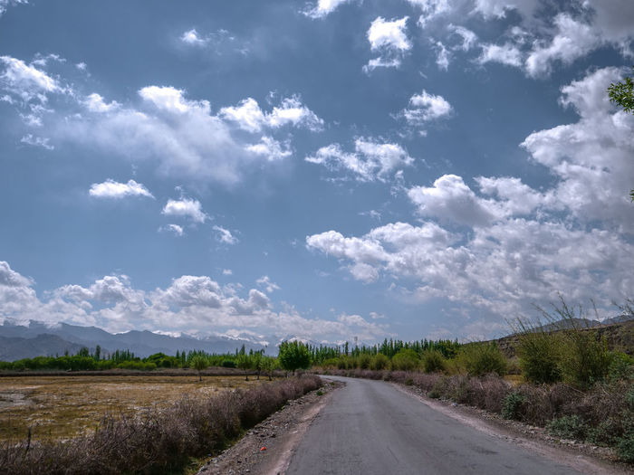 Empty road along landscape and trees against sky