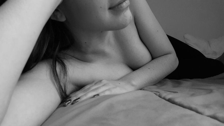 Midsection of sensuous young woman covering breasts with hand while lying on bed