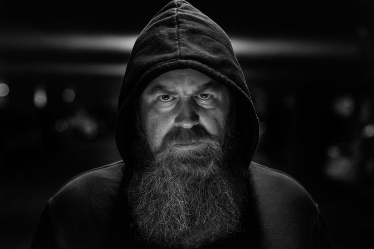 Portrait of serious bearded mature man wearing hoodie in darkroom