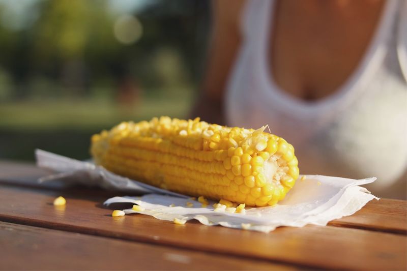 Close-up of corn with tissue paper on table with woman in background