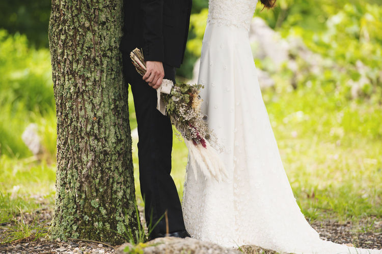 Midsection of couple standing by tree trunk