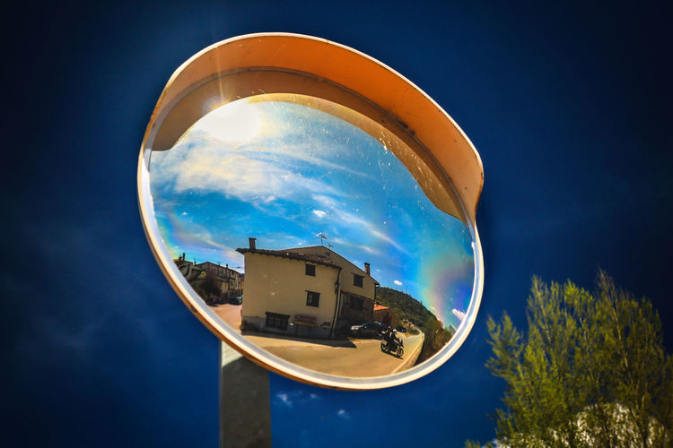 Low angle view of building reflected on a traffic mirror  against sky