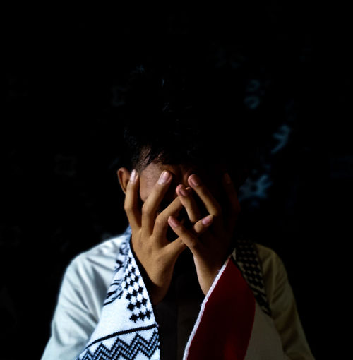 Portrait of teenage girl covering face against black background