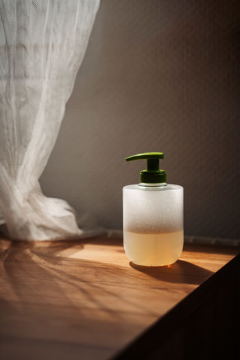 Liquid hand soap with foam and a green cap on wooden table with backlit curtain