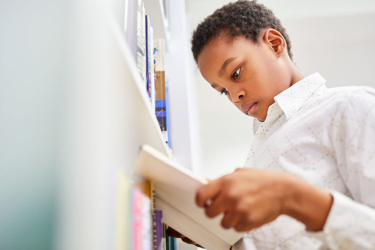 Boy reading book while standing at library