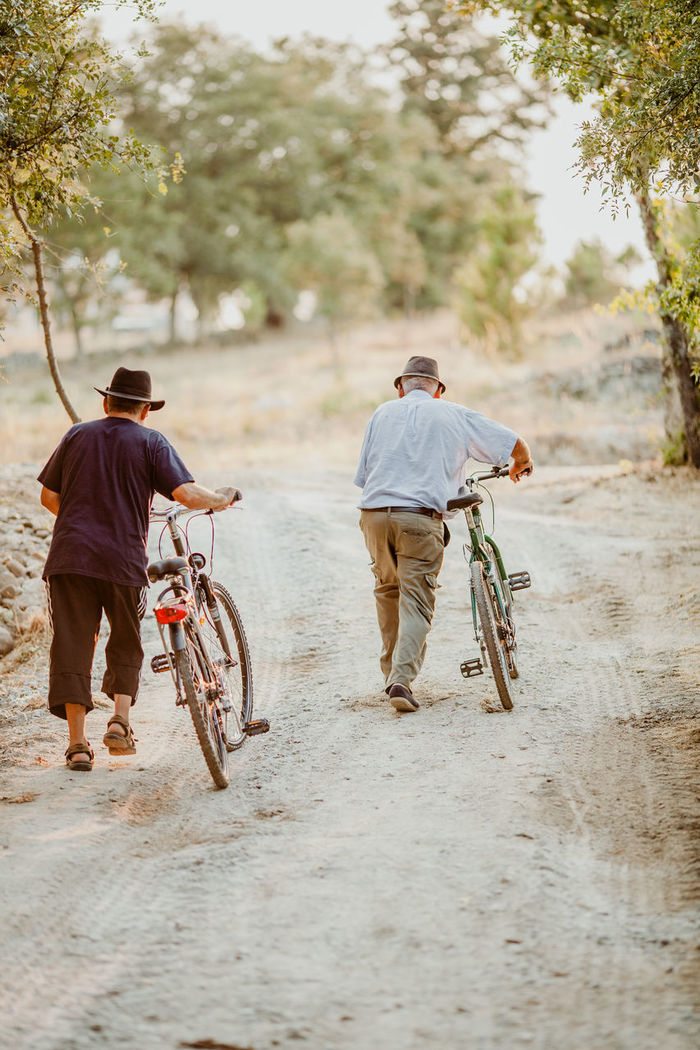 Rear view of men walking with bicycles on dirt road
