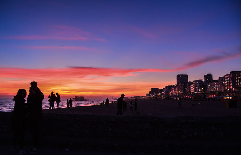 Silhouette people on beach against sky during sunset