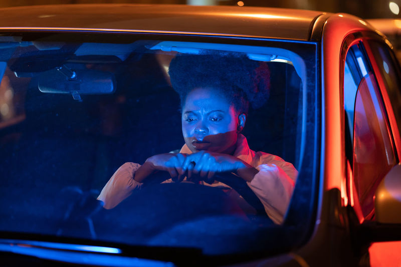 Depressed afro woman sit behind steering wheel in car at night, pondering about problems in life