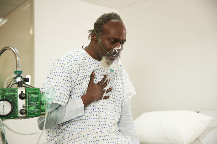 Patient touching chest wearing oxygen mask in medical room