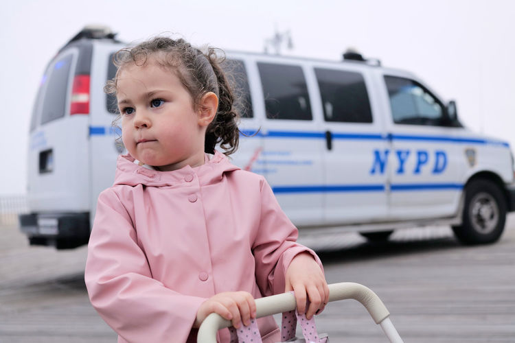 Young girl playing with her toy stroller on the boardwalk as a police van passes by