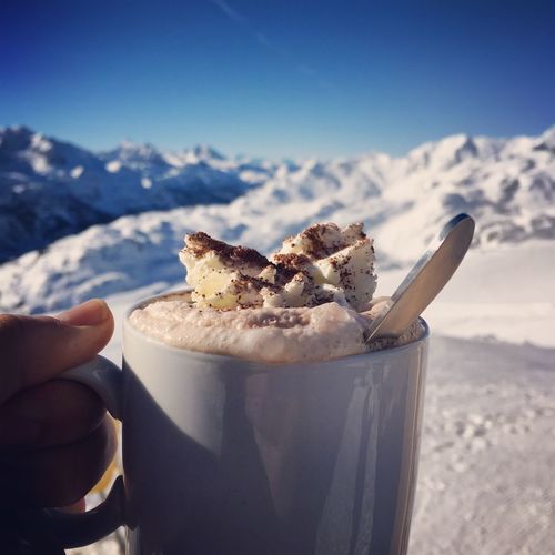 Close-up of hand holding coffee against snowy mountains