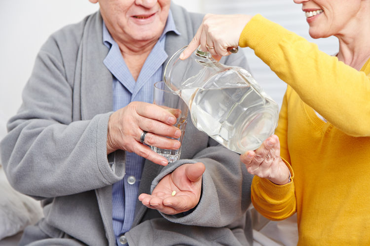 Woman giving drinking water to senior man at home