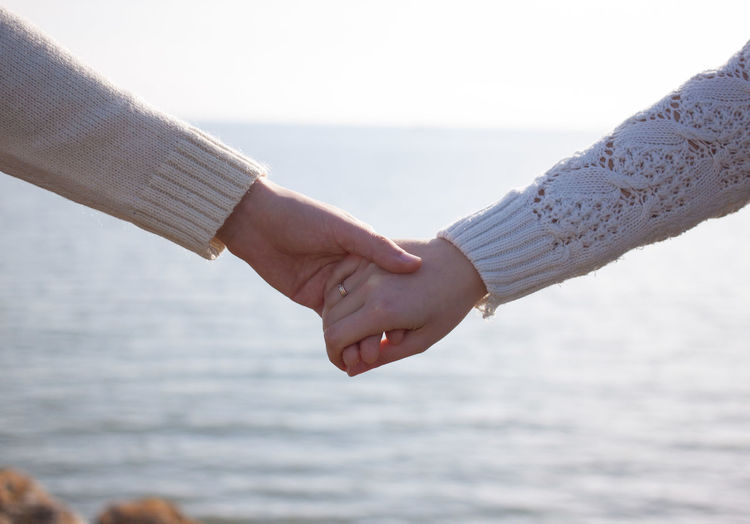Cropped image of couple holding hands against sea