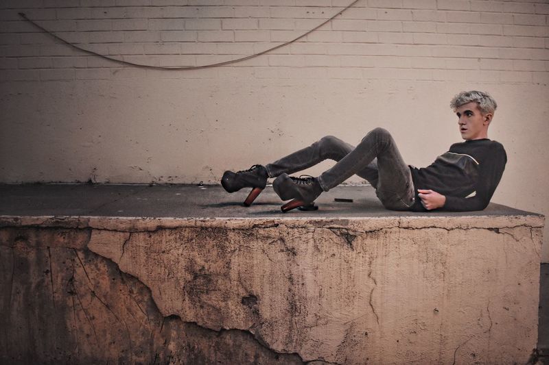 Full length of man with high heels lying against wall