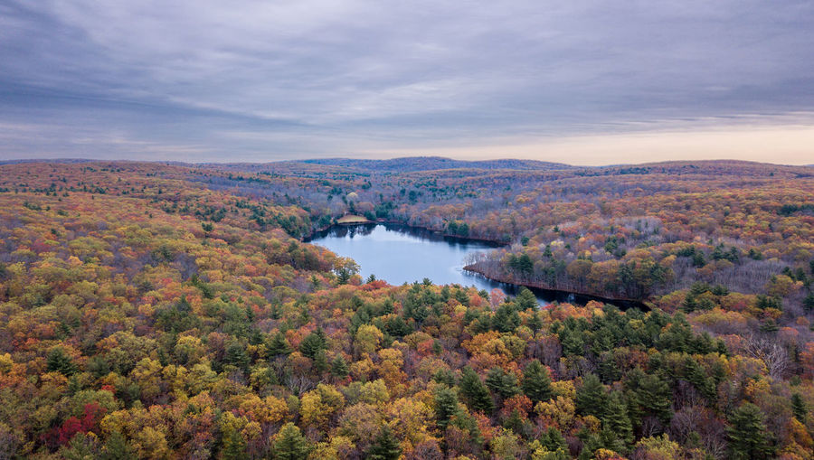 Scenic view of river amidst autumn trees against cloudy sky during sunset