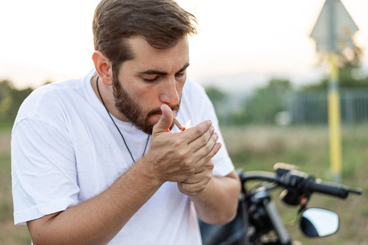 Fashionable young man sitting and smoking on a classic motorbike in sunset.