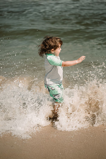 Full length of elementary boy splashing water on beach against sea