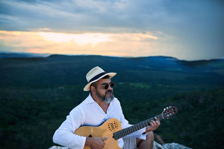 Man playing guitar on mountain against sky during sunset