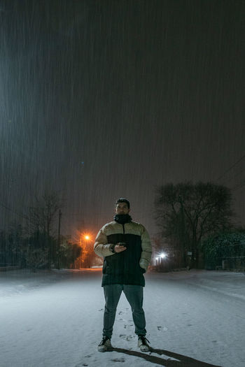 Rear view of man standing on snow covered tree at night
