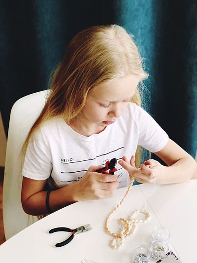High angle view of girl making bead necklace at table