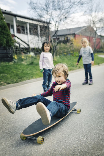 Children looking at friend skateboard on footpath outside house