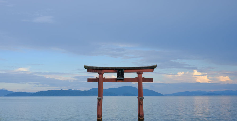 Gate of shrine on sea against sky during sunset