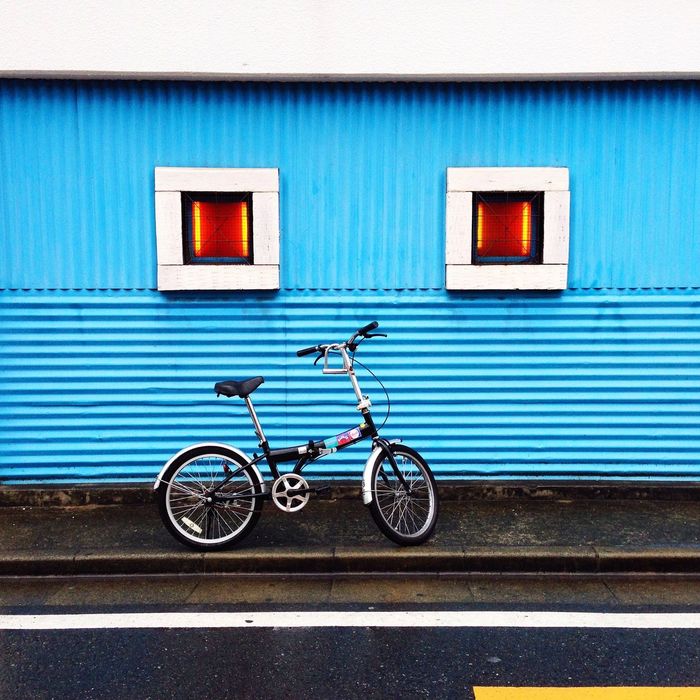 Bicycle parked against blue wall with windows