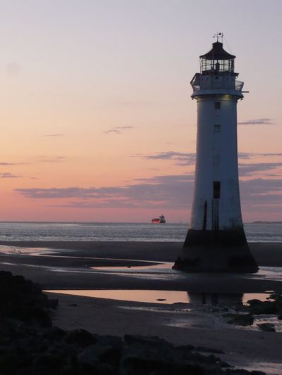 Lighthouse at beach against sky during sunset
