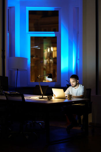 Thoughtful young businessman in glasses work on laptop at night preparing for startup presentation