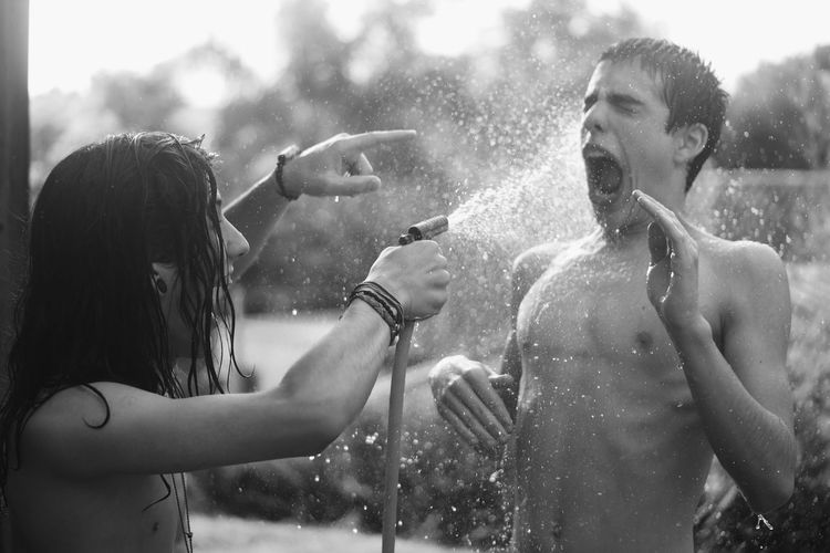Close-up of shirtless boy and girl bathing with garden hose