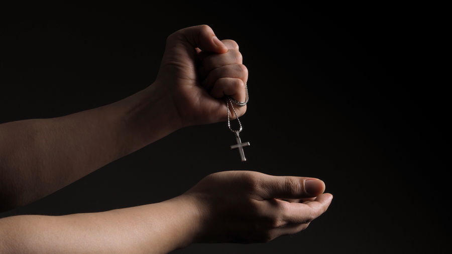 Cropped hand of woman holding cross against black background