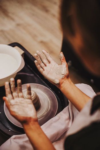 Cropped image of woman with messy hands sitting by pottery wheel