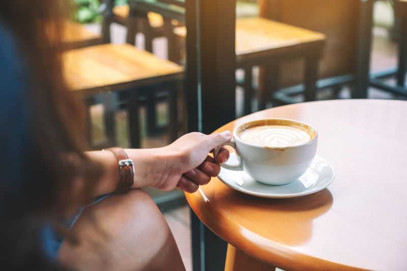 Cropped hand of woman holding coffee cup on table at cafe