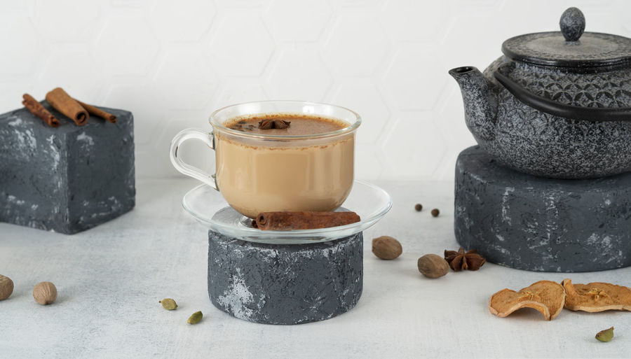 Masala tea or chai in a glass cup with traditional teapot on pedestal. indian drink with spicy, milk