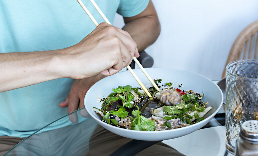 Man in blue eating chopsticks vegan food jiaozi with tofu , vegetables in soy sauce  chinese dish