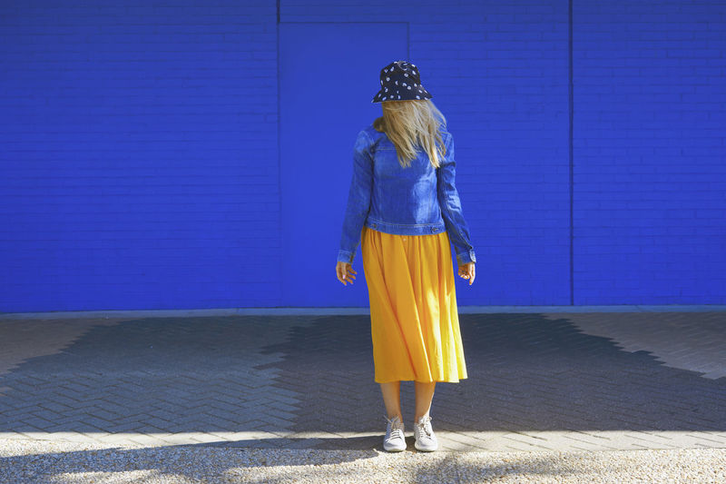 Blond woman wearing bucket hat standing in front of blue wall