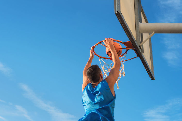 Low angle view of man playing basketball against blue sky