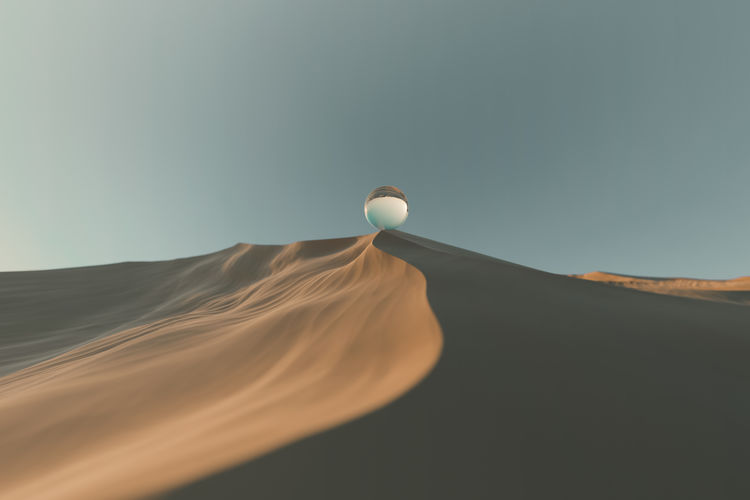Crystal ball on sand dune at desert against clear sky