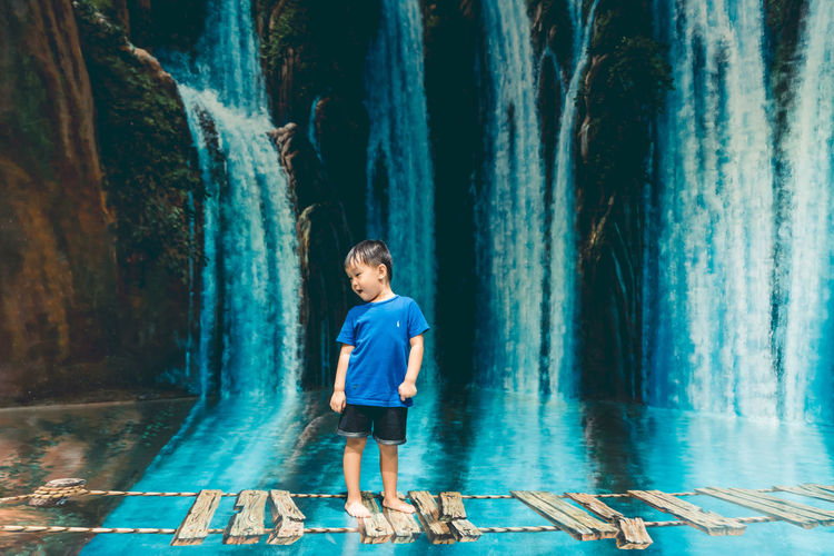 Boy standing on footbridge against waterfall