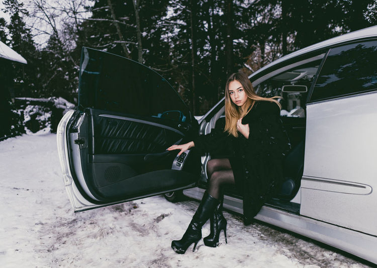Full length of young woman sitting on car seat during winter