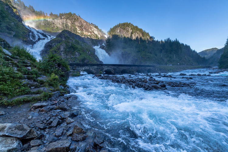 River flowing through bridge with mountains and rainbow in the distance
