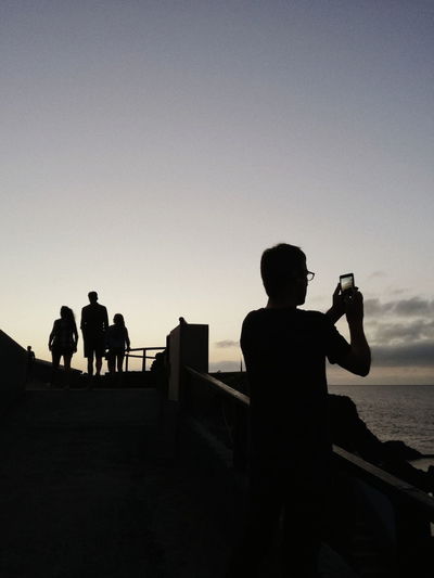 Silhouette people photographing on beach against clear sky