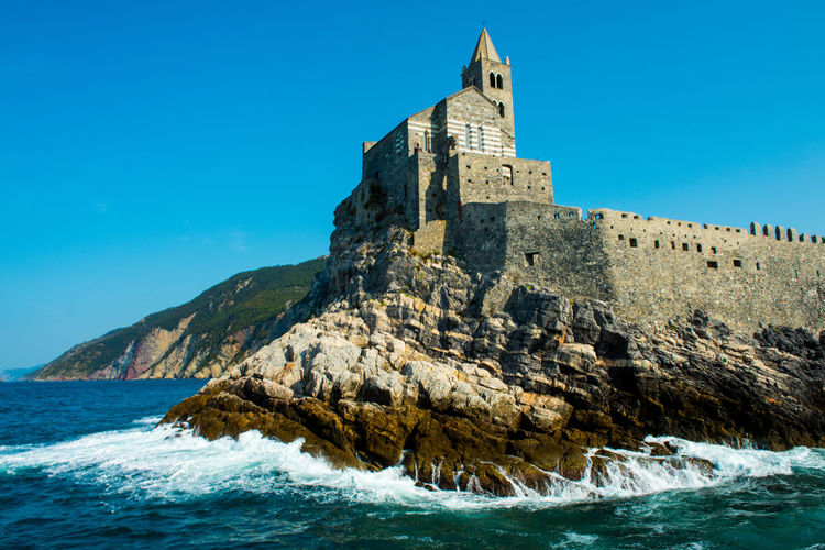 Low angle view of castle by sea against clear blue sky