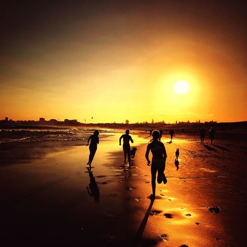 Silhouette people on beach against sky during sunset