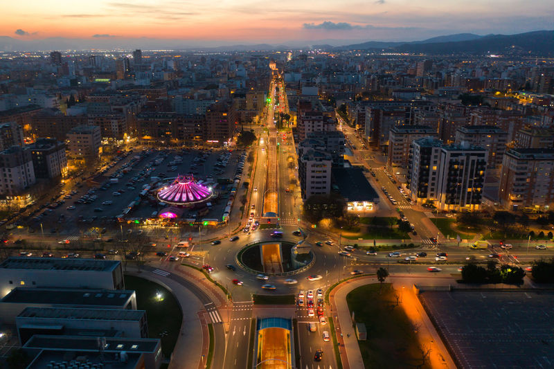 Amazing aerial view of circus tent illuminated with neon lights placed near road in city under sundown sky in spain