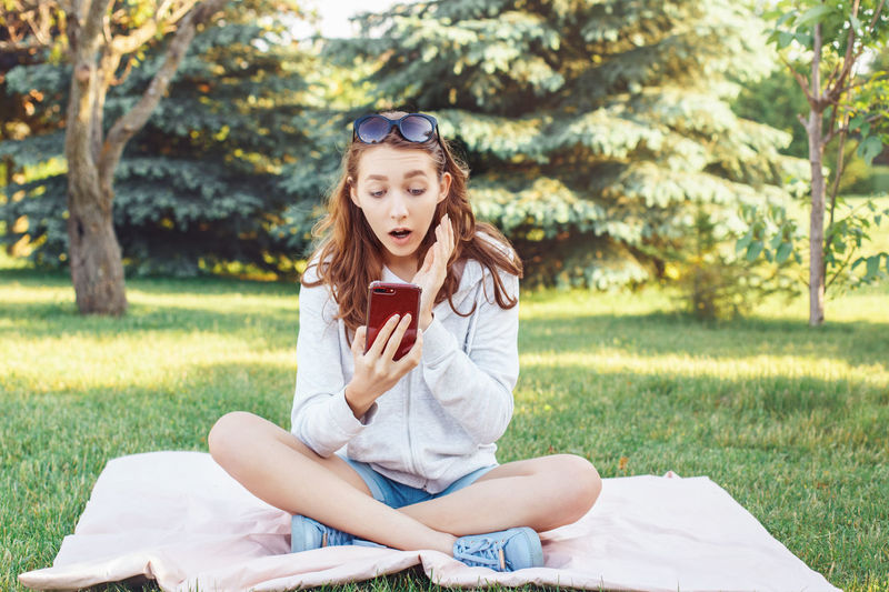 Young woman using phone while sitting on grass