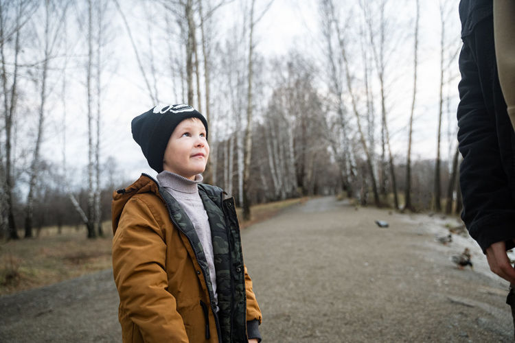 Boy standing against bare trees during winter