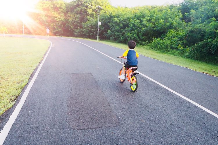 Rear view of  man riding motorcycle on road , a boy is cycling follow his mum