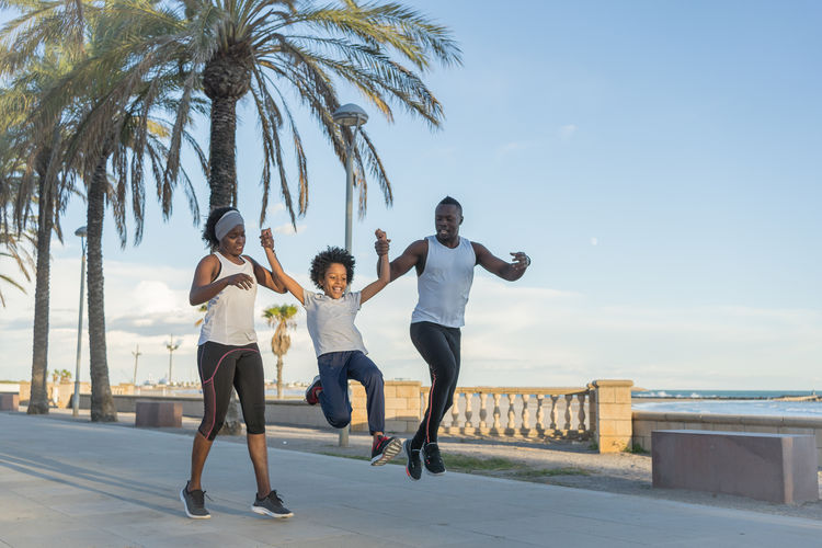 African american family in sportswear running along street while smiling and training together in summer